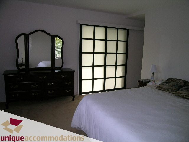 Furnished bedroom with a large bed, wooden dresser, and a window with frosted glass panels. - 94 Bonnymuir Drive, West Vancouver