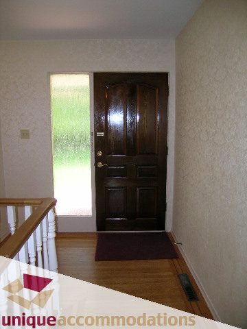 Bright hallway leading to a wooden door, hardwood floors, and a dark brown rug. - 94 Bonnymuir Drive, West Vancouver