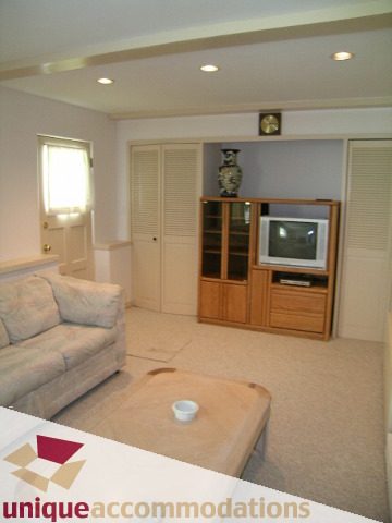Furnished living room with beige carpet, wooden entertainment center, and a white couch. - 94 Bonnymuir Drive, West Vancouver
