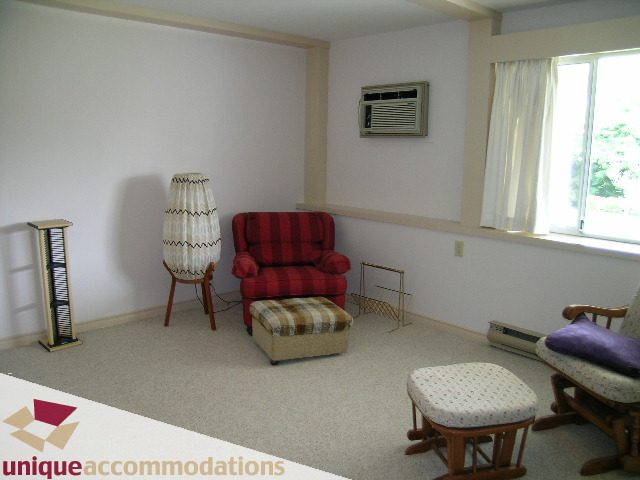Bright living room with red plaid couch, wooden floor, and large window with city view. - 94 Bonnymuir Drive, West Vancouver