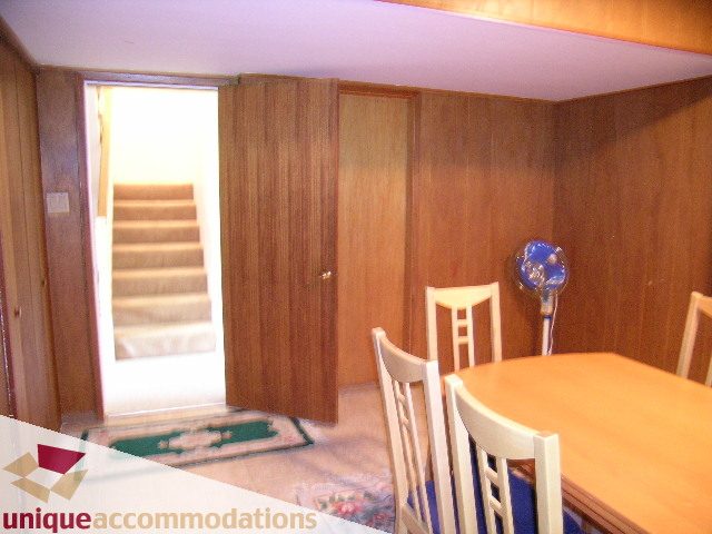 Dining area with wooden walls, chairs, and a table, leading to a staircase. - 94 Bonnymuir Drive, West Vancouver