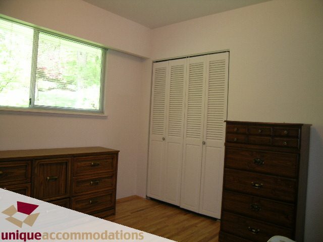Bright bedroom with wooden floors, white shutters, and a large window. - 94 Bonnymuir Drive, West Vancouver