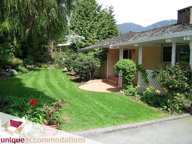 Bright living room with large windows and a cozy fireplace, surrounded by lush greenery. - 94 Bonnymuir Drive, West Vancouver
