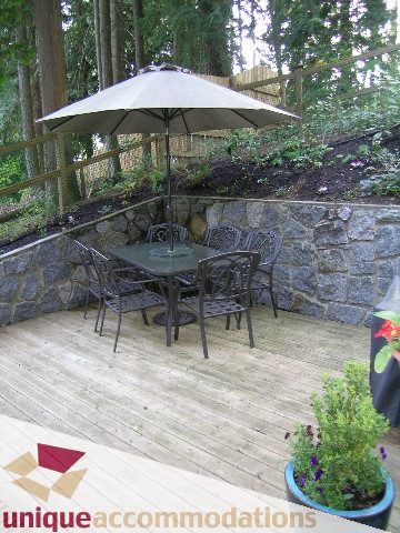Furnished patio with stone walls, wooden deck, and outdoor seating. - 1003 Kilmer Road, North Vancouver