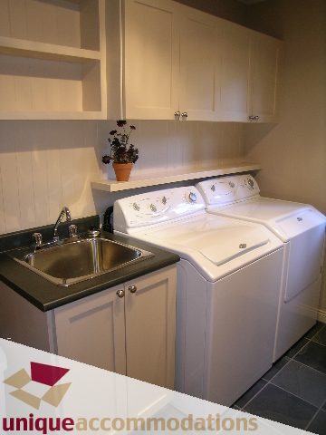 Bright laundry room with white cabinets, countertop, and stainless steel sink. - 1003 Kilmer Road, North Vancouver