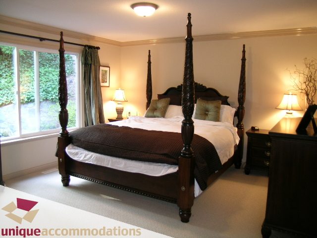 Spacious master bedroom with four-poster bed, large window, and cozy ambiance. - 1003 Kilmer Road, North Vancouver