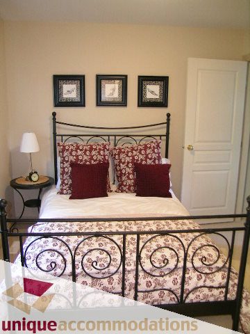 Furnished bedroom with wrought iron bed frames and red floral bedding. - 1003 Kilmer Road, North Vancouver