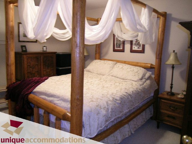 Furnished bedroom with wooden four-poster bed, white canopy, and nightstand. - 1003 Kilmer Road, North Vancouver