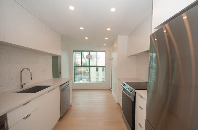 Bright kitchen with white countertops and hardwood floors, featuring a city view through the window. - 1901 - 909 Burrard Street, Vancouver Downtown