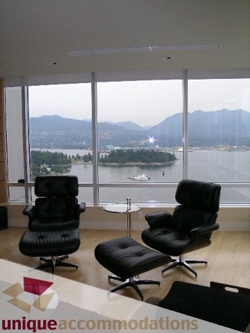 Spacious living room with a stunning city view, featuring black leather furniture and hardwood floors.