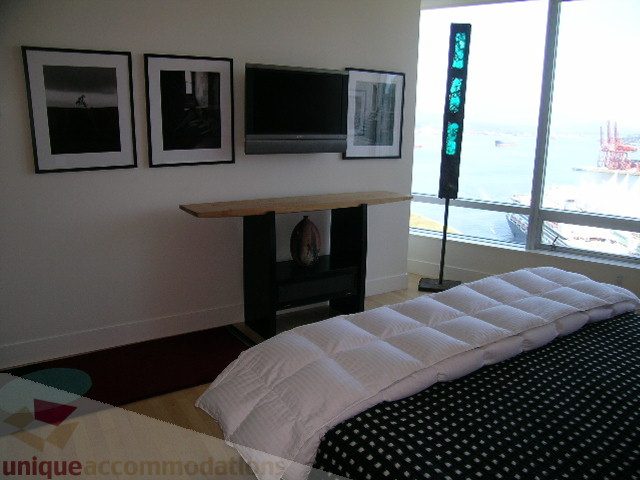 Spacious bedroom with a city view, modern decor, and a large window showcasing the waterfront. - 2401 - 1077 W. Cordova Street, Vancouver Downtown