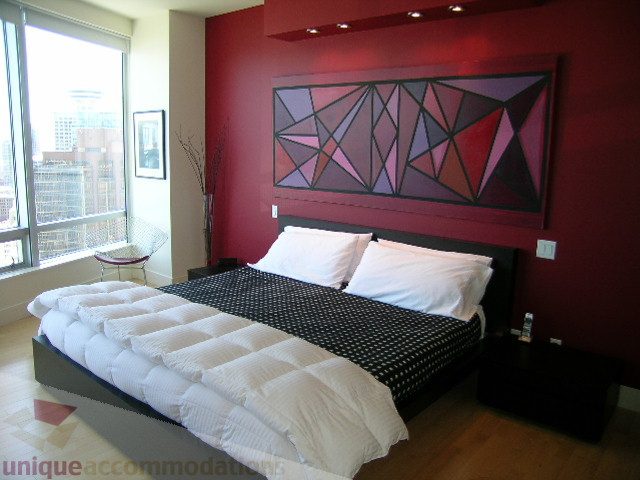 Spacious bedroom with red accent wall, geometric artwork, and city view from large window. - 2401 - 1077 W. Cordova Street, Vancouver Downtown