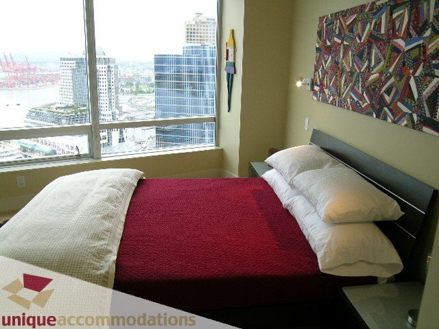 Spacious 2-bedroom condo with a stunning city view from the large window, featuring a cozy bed and vibrant artwork on the...
