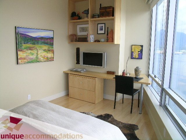 Spacious bedroom with hardwood floors, a cozy bed, and a large window offering a stunning city view.