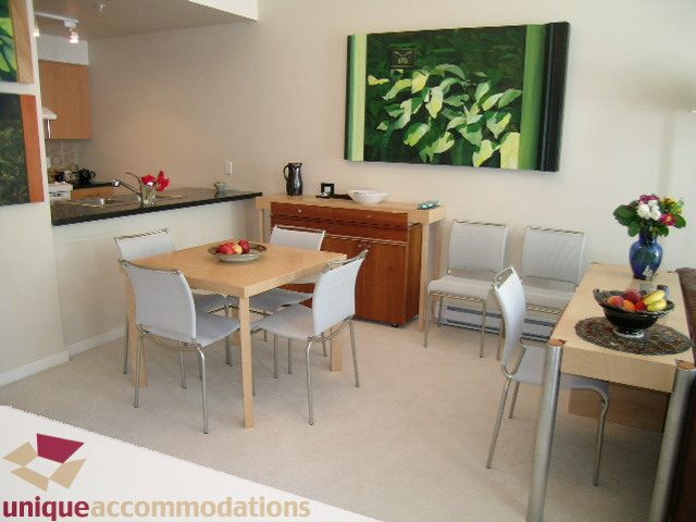Furnished dining area with wooden table, white chairs, and vibrant artwork on the wall. - 183 Aquarius Mews, Vancouver Downtown