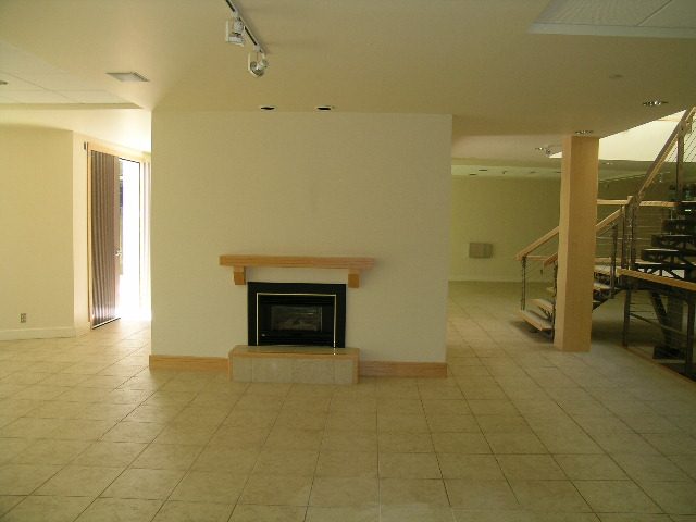 Spacious living room with tiled floor, modern fireplace, and open staircase leading to upper level. - 947 Huntingdon Crescent, North Vancouver