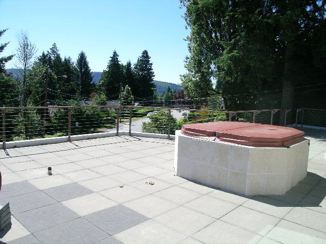 Spacious patio with stone seating and a view of greenery and mountains. - 947 Huntingdon Crescent, North Vancouver