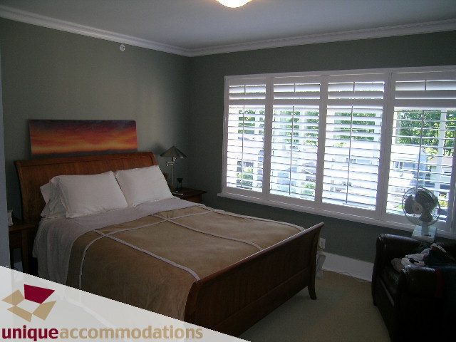 Spacious bedroom with wooden sleigh bed, large windows, and a serene city view. - 815 West 23rd Street, Vancouver West Side