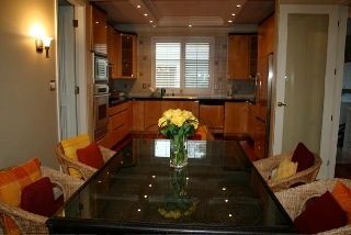 Furnished living room with modern furniture and glass coffee table, leading to a kitchen with stainless steel appliances...