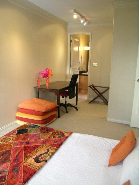 Bright bedroom with patchwork quilt and orange accents, leading to a kitchen with hardwood floors. - 1233 11th Street, West Vancouver