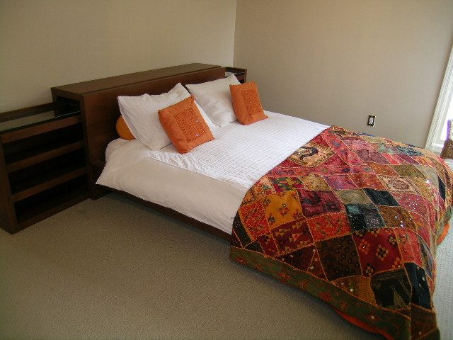 Furnished bedroom with patchwork quilt and orange pillows, hardwood floors. - 1233 11th Street, West Vancouver