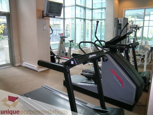 Spacious fitness room with treadmills, elliptical, and large windows offering city views. - 603 - 1328 West Pender, Vancouver Downtown
