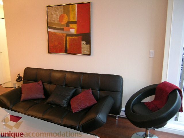 Spacious living room with modern black leather sofa, red throw pillows, and vibrant abstract art on the wall.