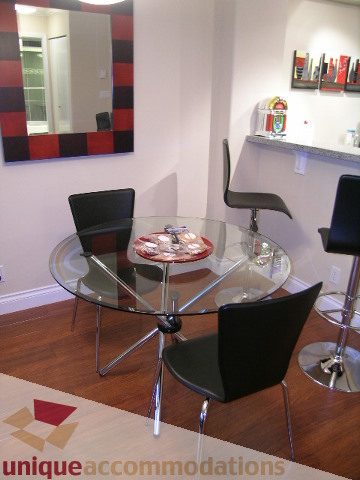 Modern dining area with glass table, black chairs, and red accent wall. - 603 - 1328 West Pender, Vancouver Downtown