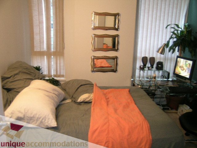 Spacious bedroom with mirrored wall decor and orange throw, perfect for a cozy stay. - 1306-388 Drake St, Vancouver Downtown