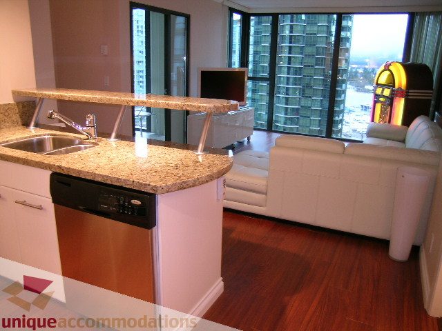 Bright kitchen with granite countertops and hardwood floors, showcasing a city view from the living area.