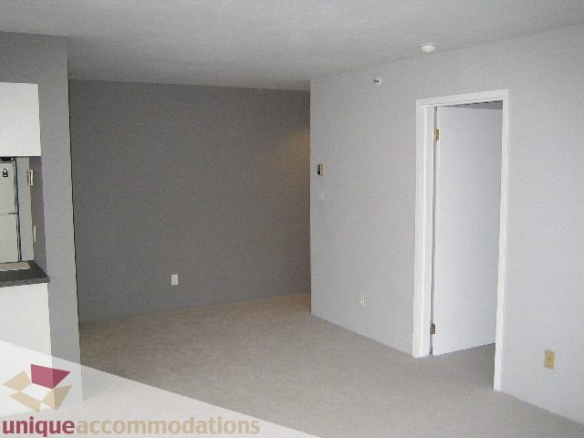 Bright living room with white walls and carpeted floor, adjacent to a kitchen area. - 1906 - 1060 Alberni Street, Vancouver Downtown