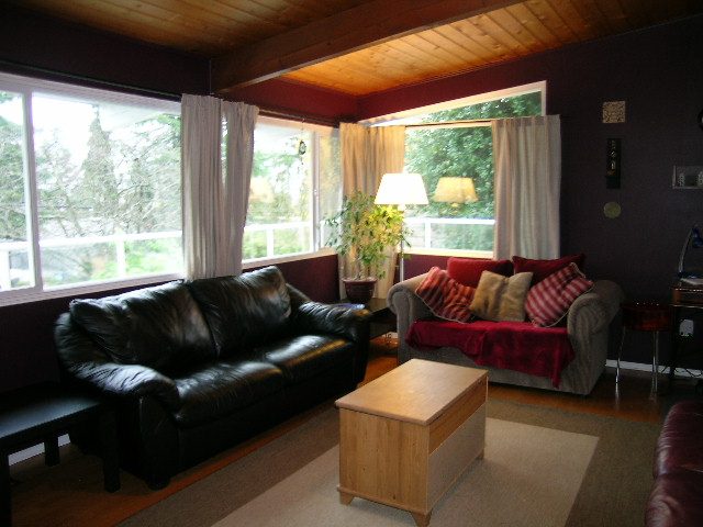 Spacious living room with leather couches, hardwood floors, and large windows with a view of greenery. - 433 Fairway Drive, North Vancouver