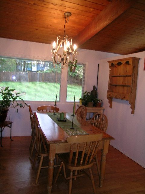 Dining room with wooden table, chairs, and chandelier, hardwood floors, and view of greenery outside. - 433 Fairway Drive, North Vancouver