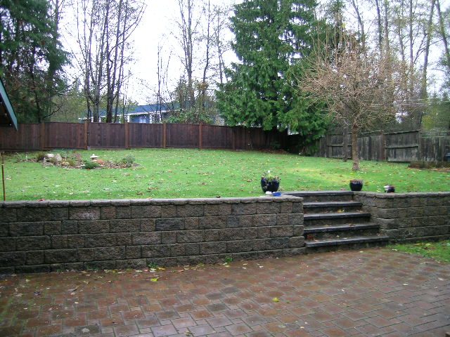 Landscaped backyard with stone retaining wall and grassy area. - 433 Fairway Drive, North Vancouver