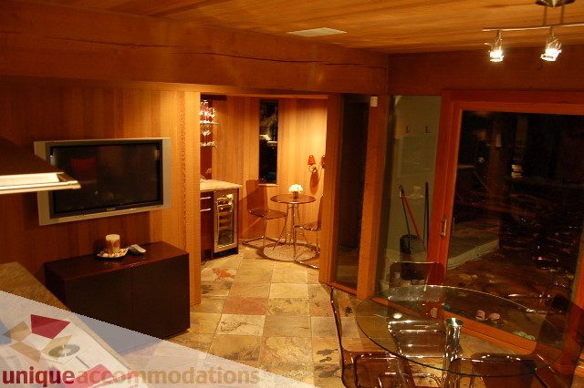 Furnished living room with wood-paneled walls, modern TV, and glass coffee table. - 6290 Collingwood Street, Vancouver West Side