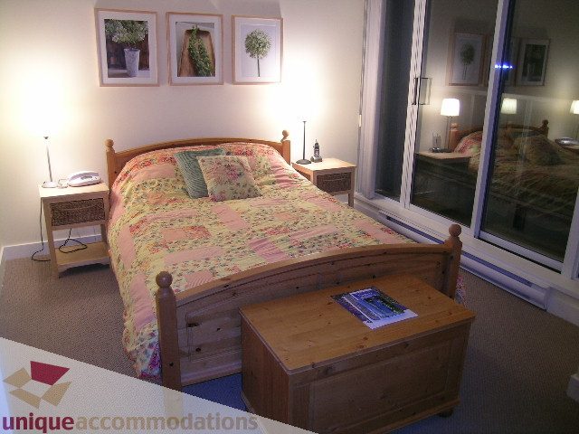 Furnished bedroom with wooden furniture, cozy bedding, and a view of the city outside. - 1430 Strathmore Mews, Vancouver Downtown