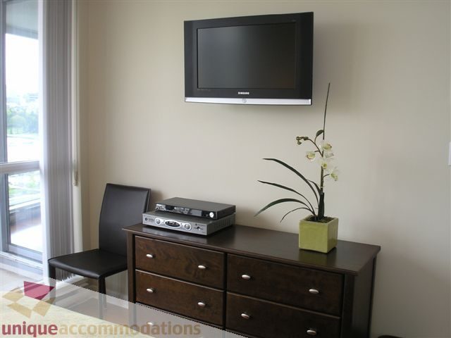 Spacious living room with dark wood dresser, flat-screen TV, and city view from large window. - 1008 - 1408 Strathmore Mews, Vancouver Downtown