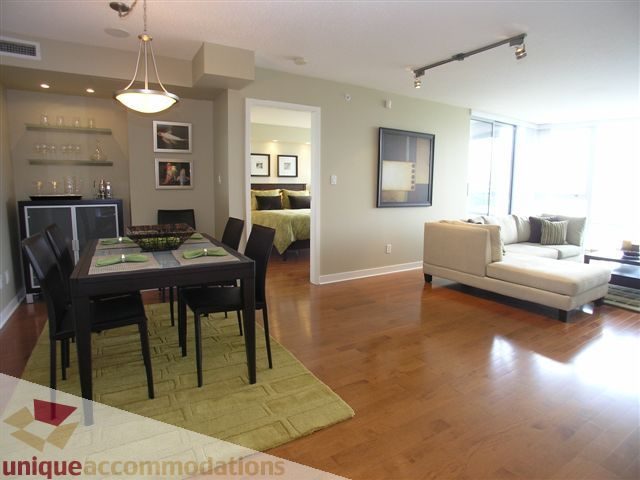 Spacious open-concept living room with hardwood floors, a cozy sectional, and a dining area with a green rug.