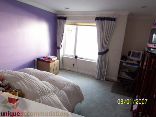 Bright bedroom with purple walls, white bedding, and a large window with curtains. - 1659 Langton Place, West Vancouver