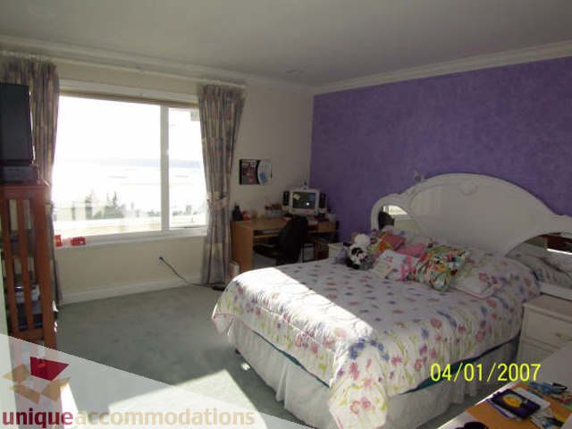Bright bedroom with purple accent wall, floral bedding, and city view. - 1659 Langton Place, West Vancouver