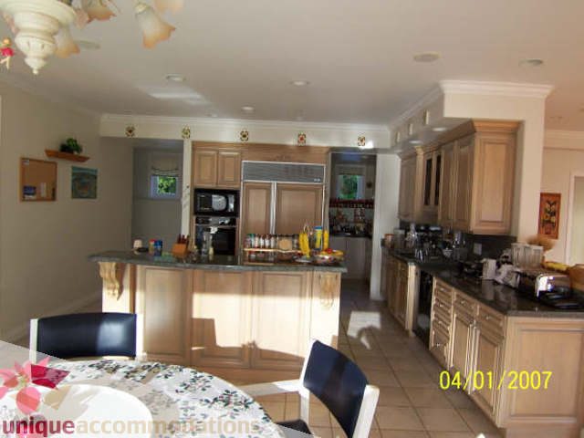 Bright kitchen with wooden cabinets, granite countertops, and a dining area with floral tablecloth. - 1659 Langton Place, West Vancouver