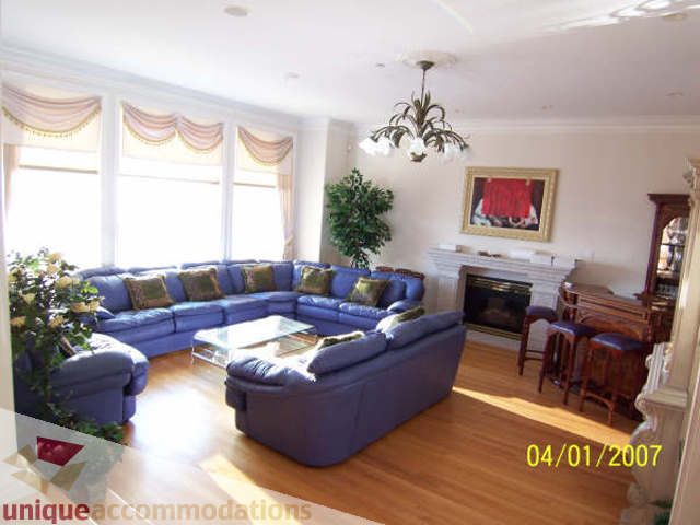 Spacious living room with hardwood floors, blue couches, and large windows. - 1659 Langton Place, West Vancouver