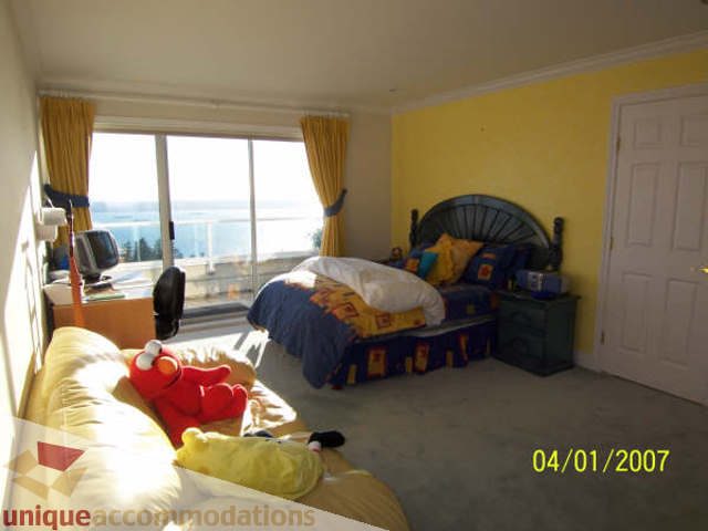 Bright bedroom with a city view, yellow walls, and a bed adorned with colorful pillows. - 1659 Langton Place, West Vancouver