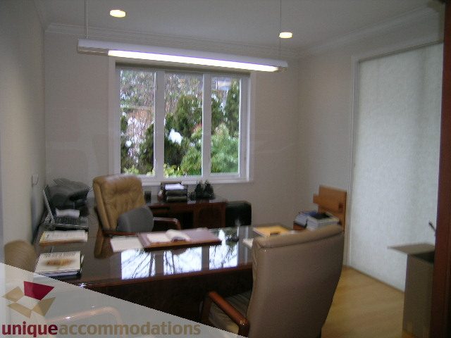 Furnished living room with hardwood floors and large windows showing greenery. - 1659 Langton Place, West Vancouver