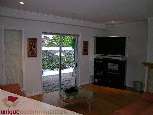 Living room with hardwood floors, glass coffee table, and sliding glass door leading to garden. - 1659 Langton Place, West Vancouver