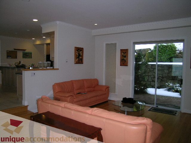 Spacious living room with orange leather couches, hardwood floors, and a view of greenery outside. - 1659 Langton Place, West Vancouver