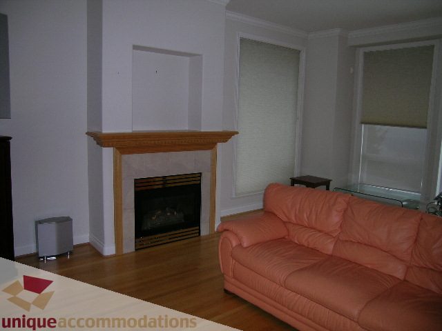 Furnished living room with hardwood floors, orange couch, and wooden mantel. - 1659 Langton Place, West Vancouver