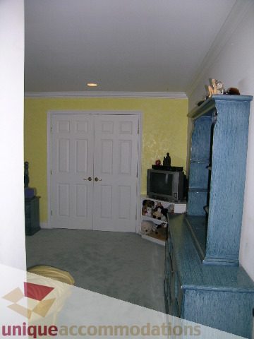 Bright living room with blue furniture and a TV, light yellow walls, and a white door. - 1659 Langton Place, West Vancouver