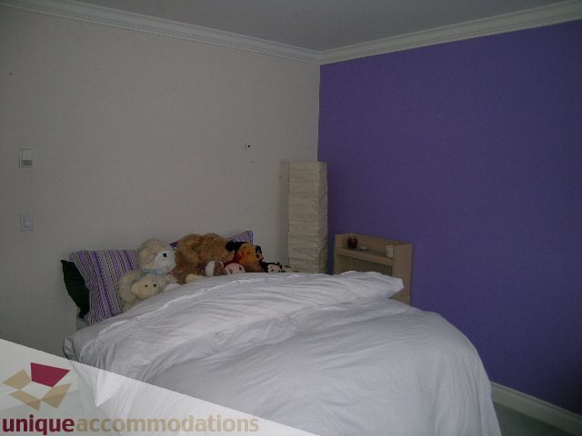 Furnished bedroom with purple accent wall and stuffed animals on bed. - 1659 Langton Place, West Vancouver