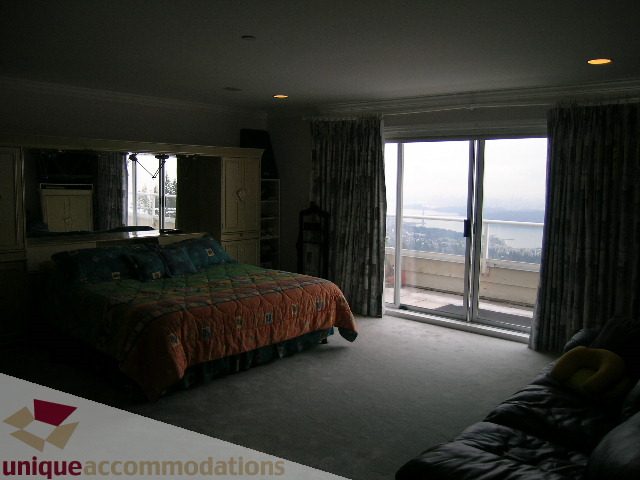 Spacious bedroom with two queen beds, city view, and large windows. - 1659 Langton Place, West Vancouver